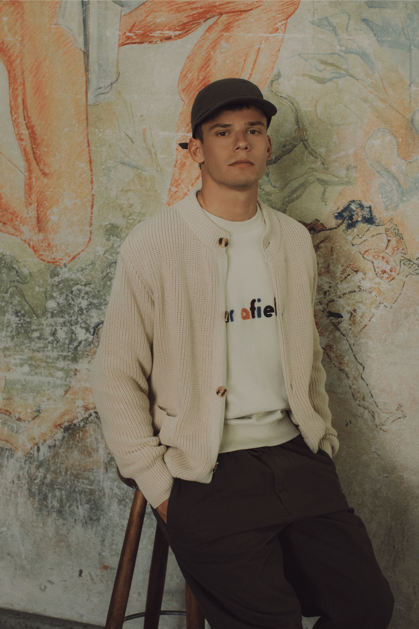 Menswear Lifestyle - Man in knitted cardigan against a textured wall with abstract art.