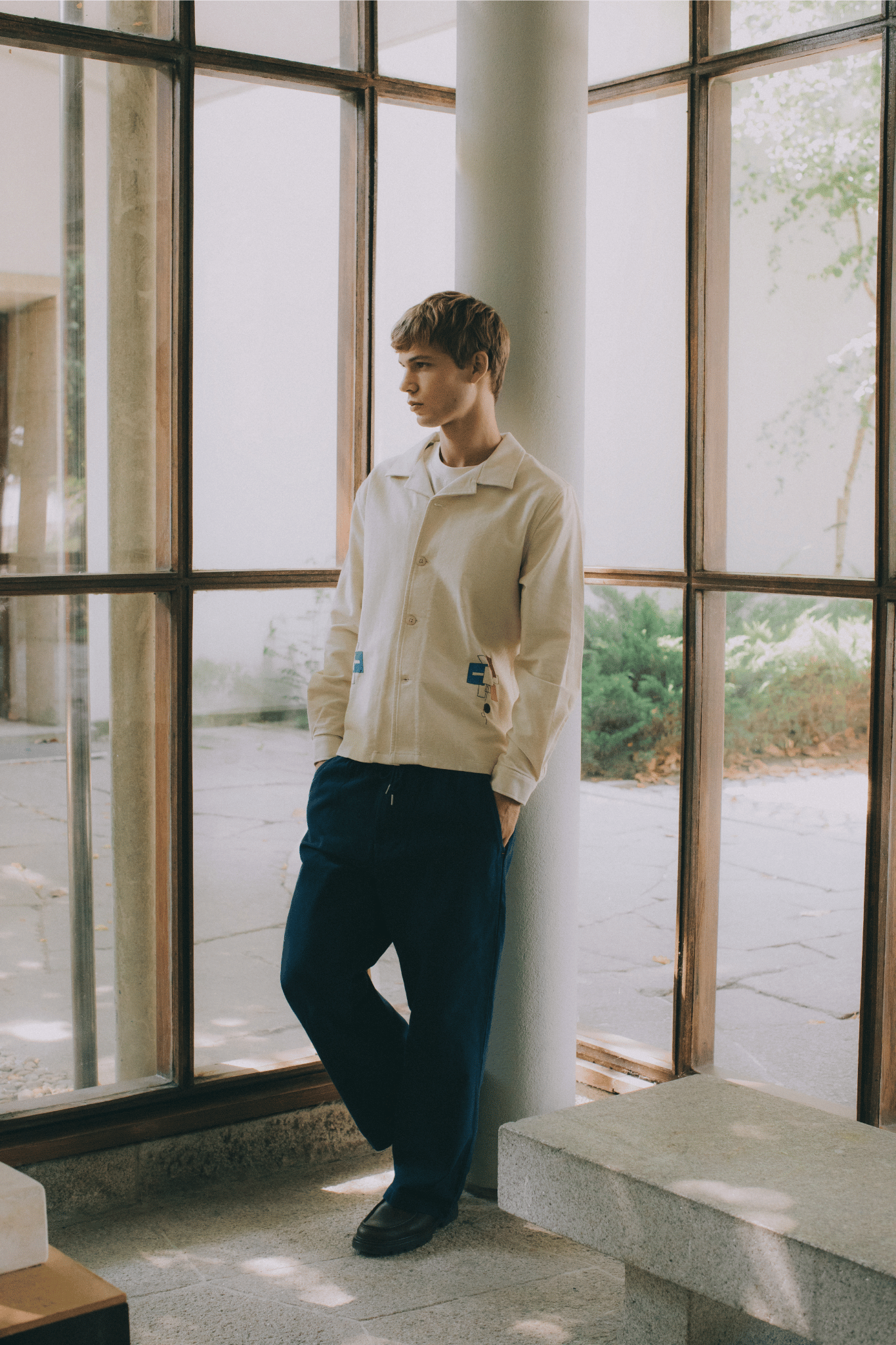 Menswear Lifestyle - Man wearing open-collar embroidered shirt in a mid-centurty modern indoor setting with large windows