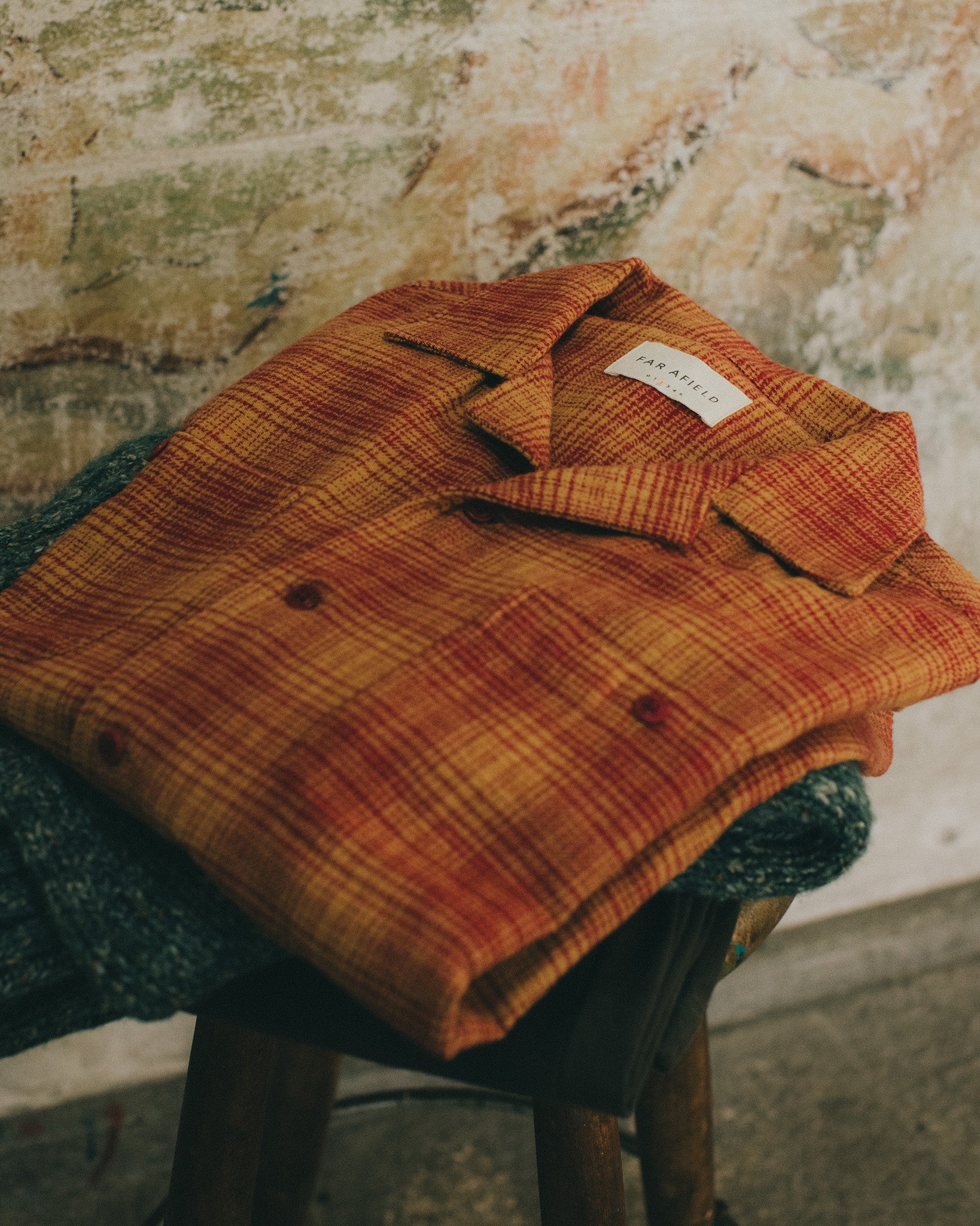 Folded orange plaid camp-collar shirt on a wooden stool, layered over a chunky knit